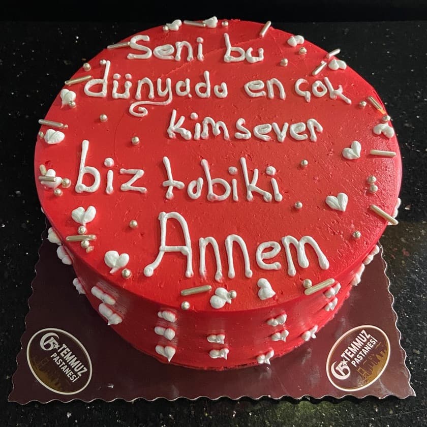 Kırmızı kremalı, üzerinde beyaz yazı ve kalpler olan yuvarlak pasta